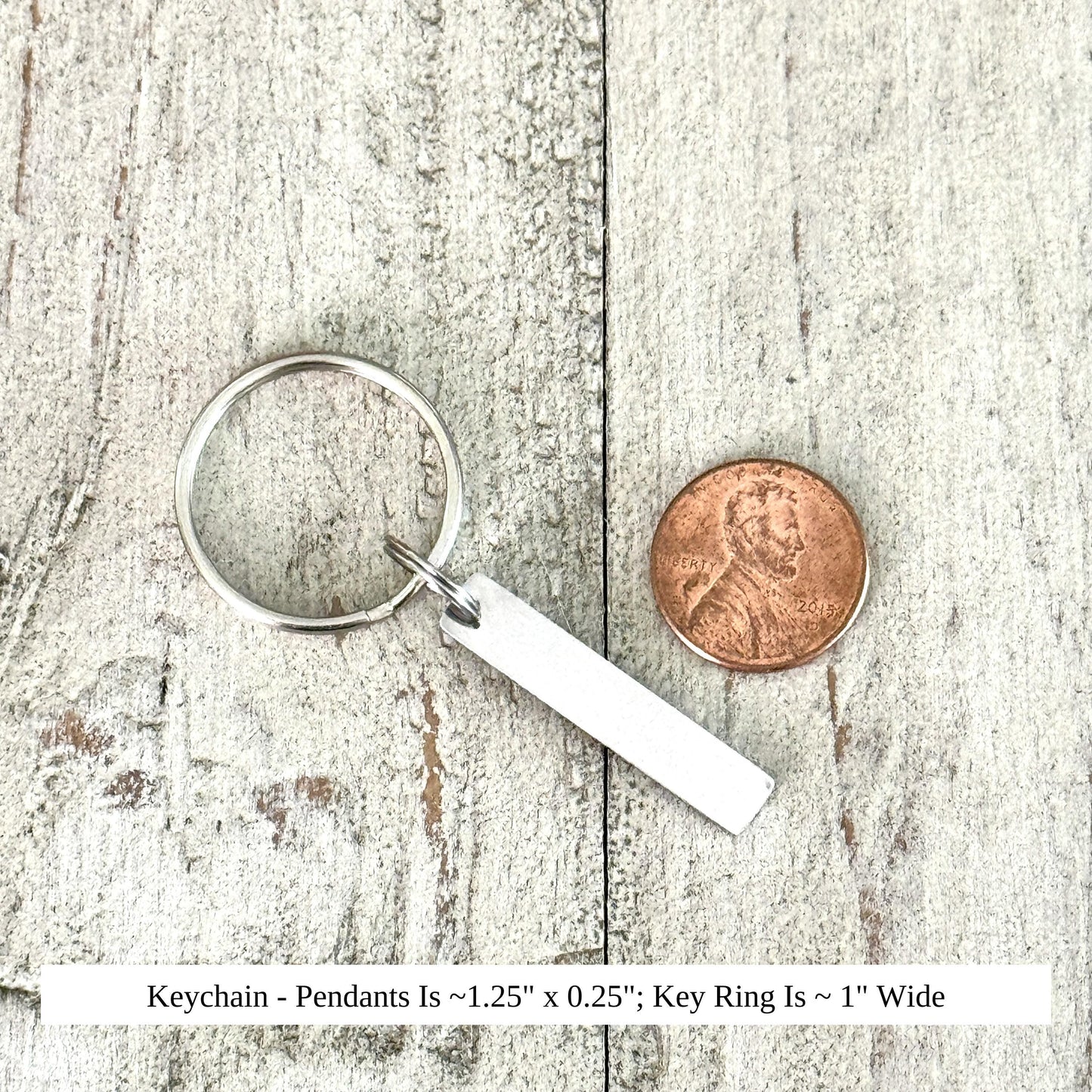 A silver keychain with a pendant and a penny coin are placed on a wooden surface.