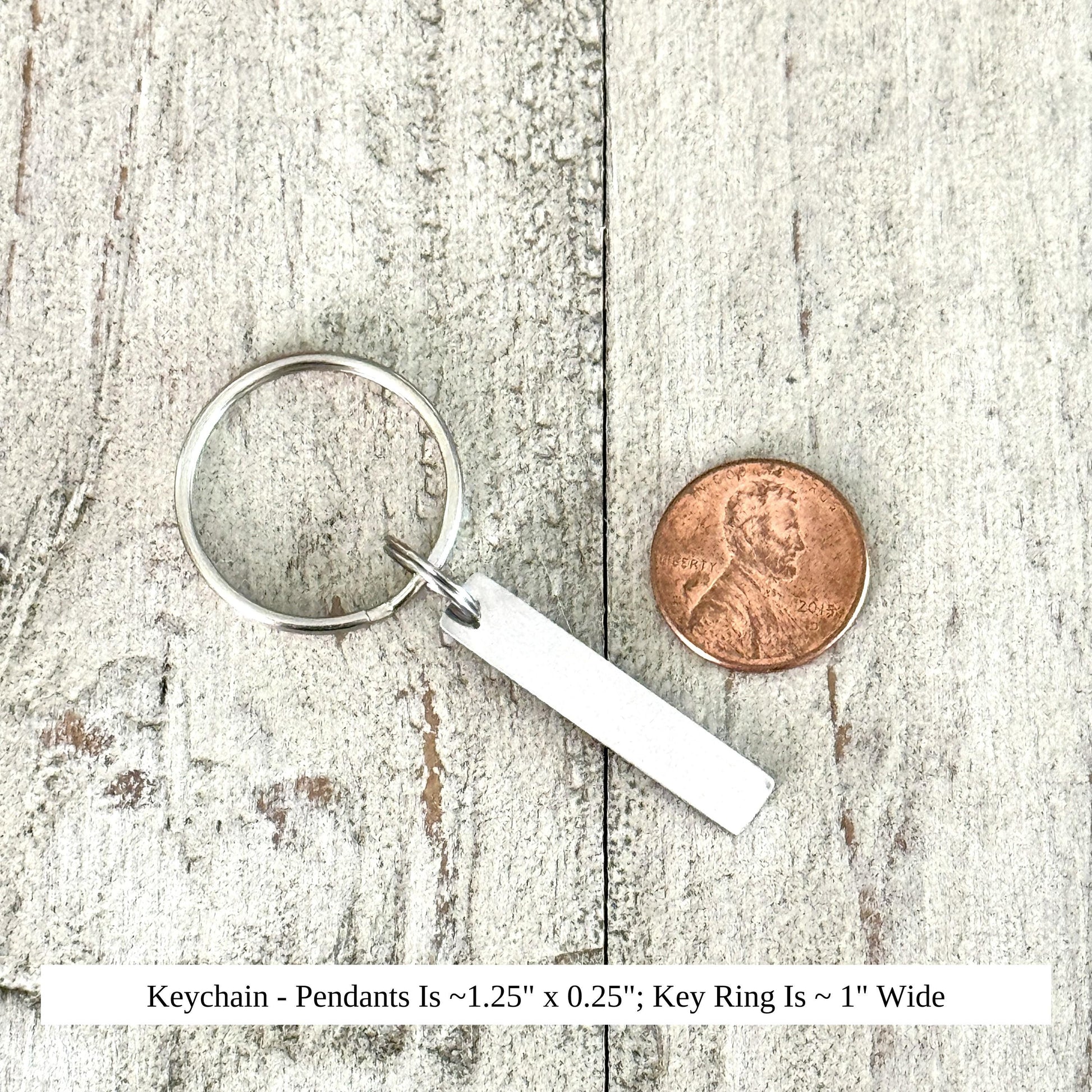 A silver keychain with a pendant and a penny coin are placed on a wooden surface.